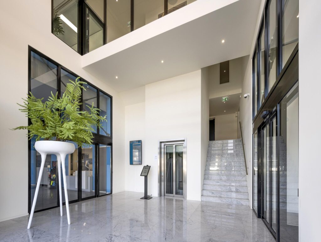 Moderne entreehal aan de Dynamostraat met marmeren vloer, glazen deuren, een lift en een grote plant in een witte designpot.