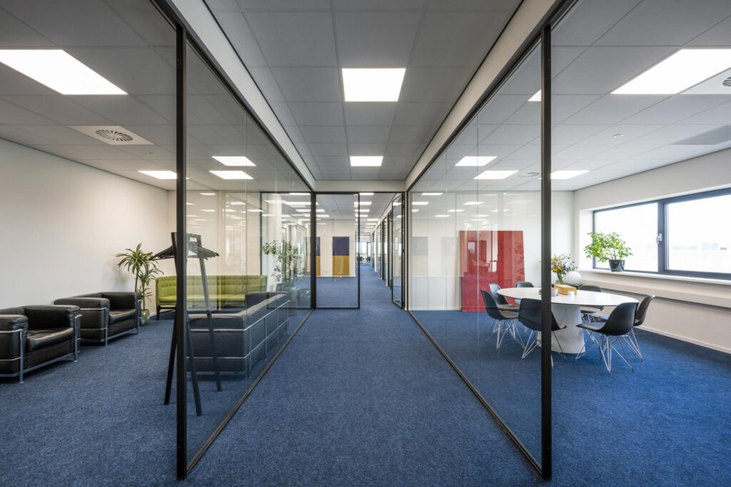 Moderne kantoorruimte aan de Dynamostraat met glazen wanden, blauwe vloerbedekking en een vergaderruimte met uitzicht.