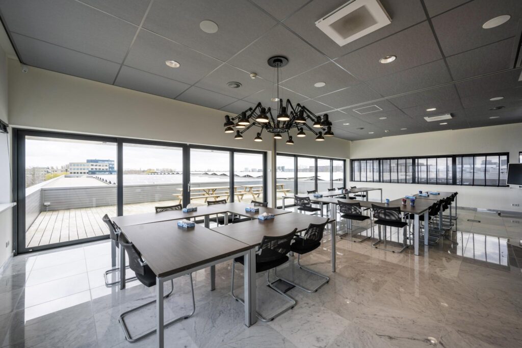 Moderne vergaderruimte aan de Dynamostraat met grote ramen, designverlichting en uitzicht op een dakterras met picknicktafels.