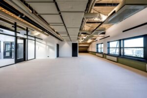 Leeg industrieel kantoorinterieur aan de Singaporestraat met zicht op plafondleidingen en grote ramen.