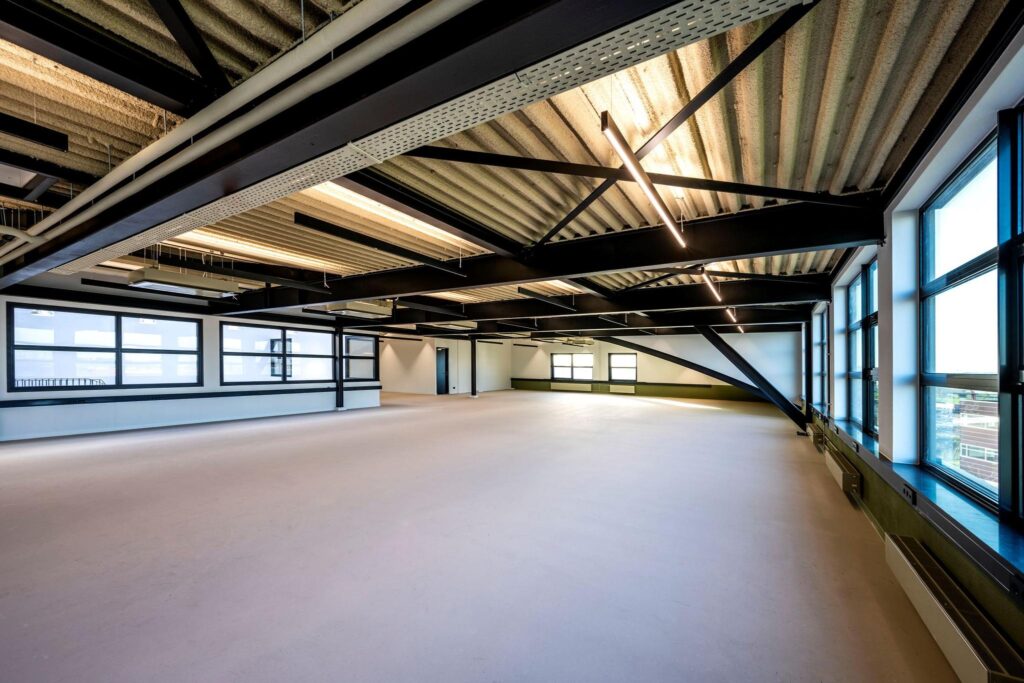 Ruime, moderne en lege kantoorruimte aan de Singaporestraat met zichtbare plafondbalken en grote ramen.