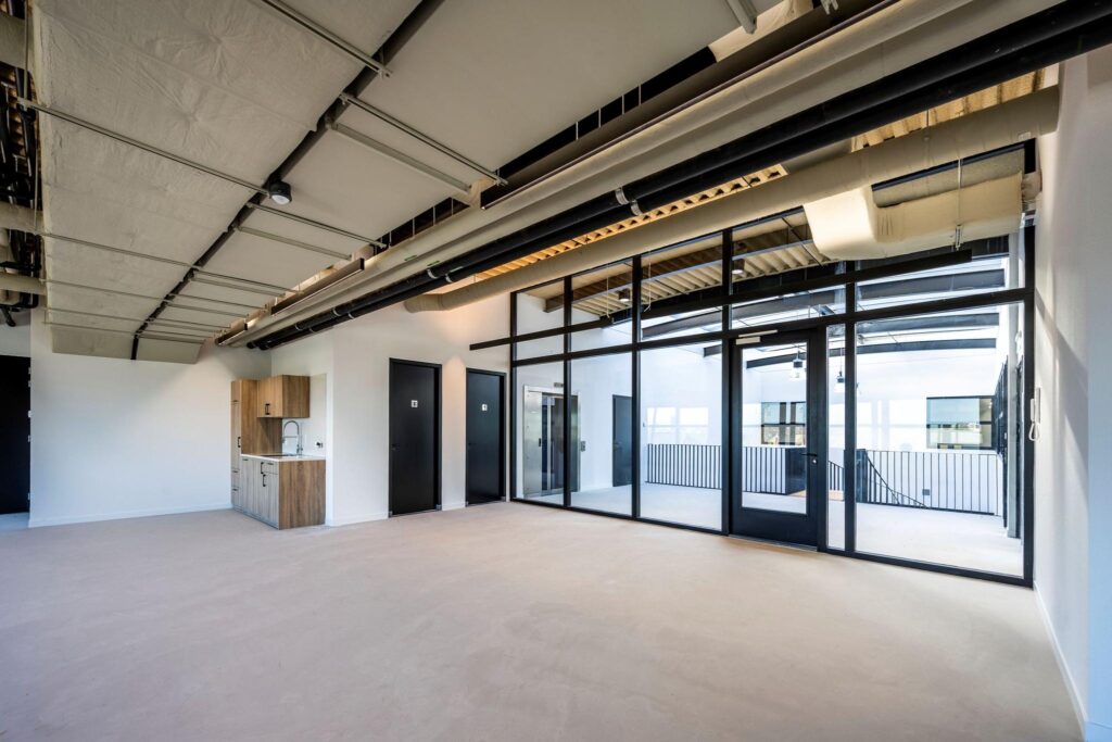 Moderne, lege kantoorruimte aan de Singaporestraat met glazen wanden, zicht op een binnenplaats, een kitchenette en zichtbare plafondleidingen.