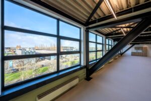 Licht industrieel kantoorinterieur met grote ramen en uitzicht op bedrijven aan de Singaporestraat.
