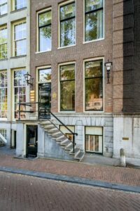 Gevel van een klassiek Amsterdams grachtenpand aan de Herengracht met trap en zwarte voordeur.
