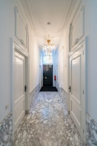 Chique entreehal aan de Herengracht met marmeren vloer, hoge witte deuren en een kristallen kroonluchter.