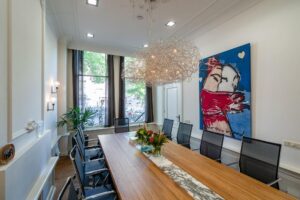 Vergaderruimte aan de Herengracht met een modern houten tafel, designstoelen, opvallende kunst van Herman Brood en groot raam met uitzicht op de gracht.