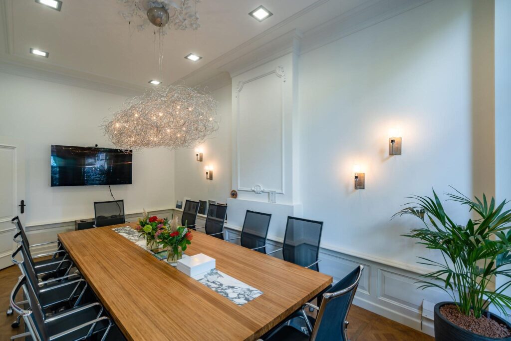 Vergaderruimte aan de Herengracht met een lange houten tafel, moderne stoelen, een grote hanglamp en een flatscreen aan de muur.