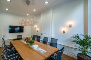 Vergaderruimte aan de Herengracht met een lange houten tafel, moderne stoelen, een grote hanglamp en een flatscreen aan de muur.
