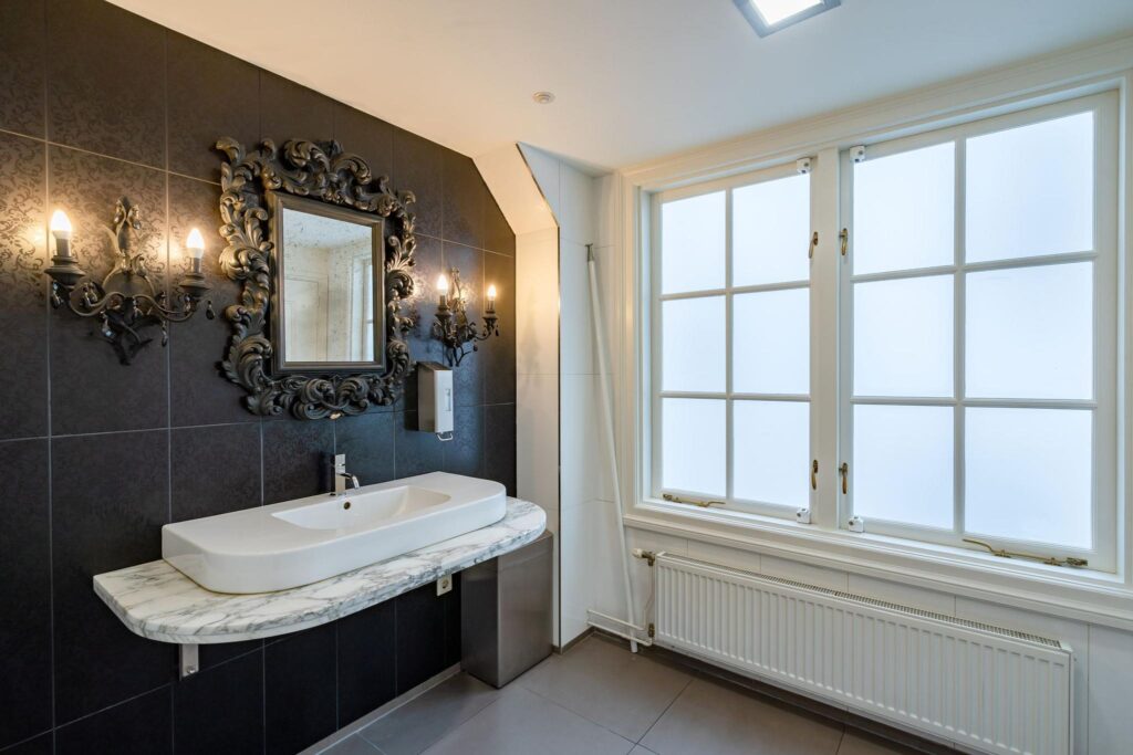 Luxe badkamer met zwart betegelde wand, marmeren wastafel en sierlijke spiegelverlichting aan de Herengracht.