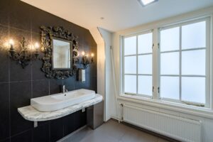 Luxe badkamer met zwart betegelde wand, marmeren wastafel en sierlijke spiegelverlichting aan de Herengracht.