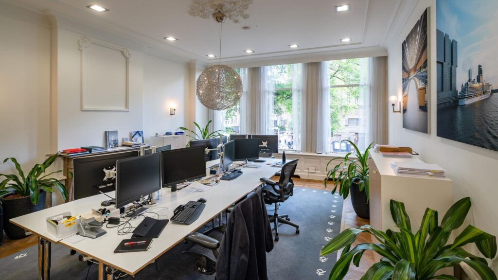 Modern ingericht kantoor aan de Herengracht met meerdere werkplekken, grote ramen en groenvoorziening.