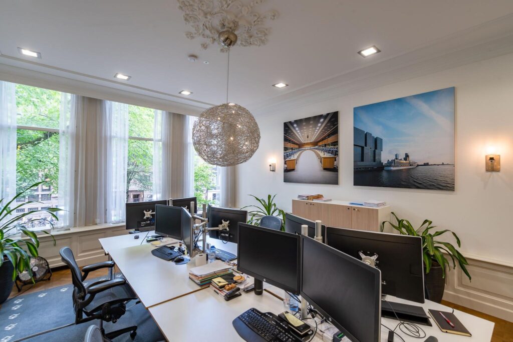 Modern kantoorinterieur aan de Herengracht met werkplekken, grote ramen en wanddecoratie van stedelijke foto's.