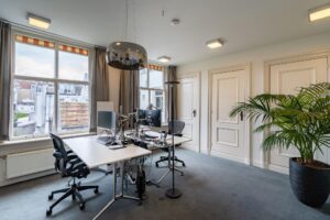 Modern ingericht kantoor aan de Herengracht met twee bureaus, computerschermen, een grote hanglamp en een kamerplant.