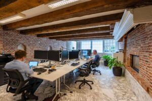 Moderne kantoorruimte aan de Herengracht met zichtbare houten balken, bakstenen muren en werkplekken met computers.