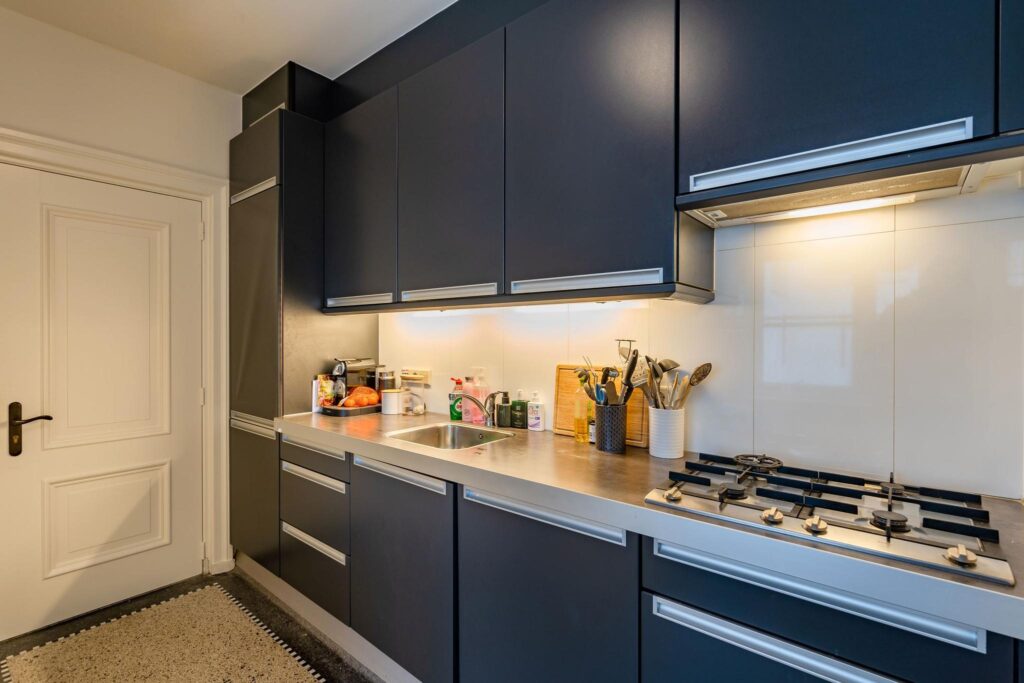 Moderne keuken met donkerblauwe kasten, een strak aanrechtblad en ingebouwde gaskookplaat aan de Herengracht.