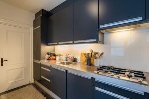 Moderne keuken met donkerblauwe kasten, een strak aanrechtblad en ingebouwde gaskookplaat aan de Herengracht.