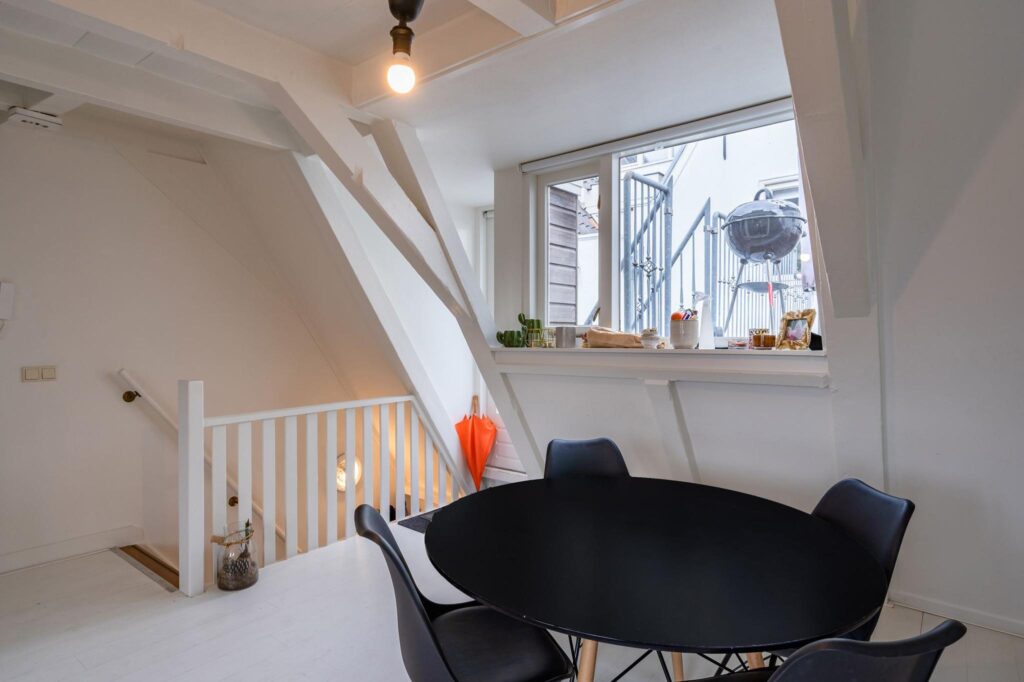 Moderne eethoek met zwarte tafel en stoelen in een lichte kamer aan de Herengracht, met uitzicht op een buitentrap en barbecue.