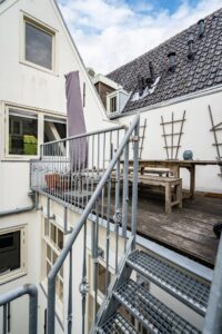 Buitenterras met houten tafel en metalen trap aan de achterzijde van een woning aan de Herengracht.