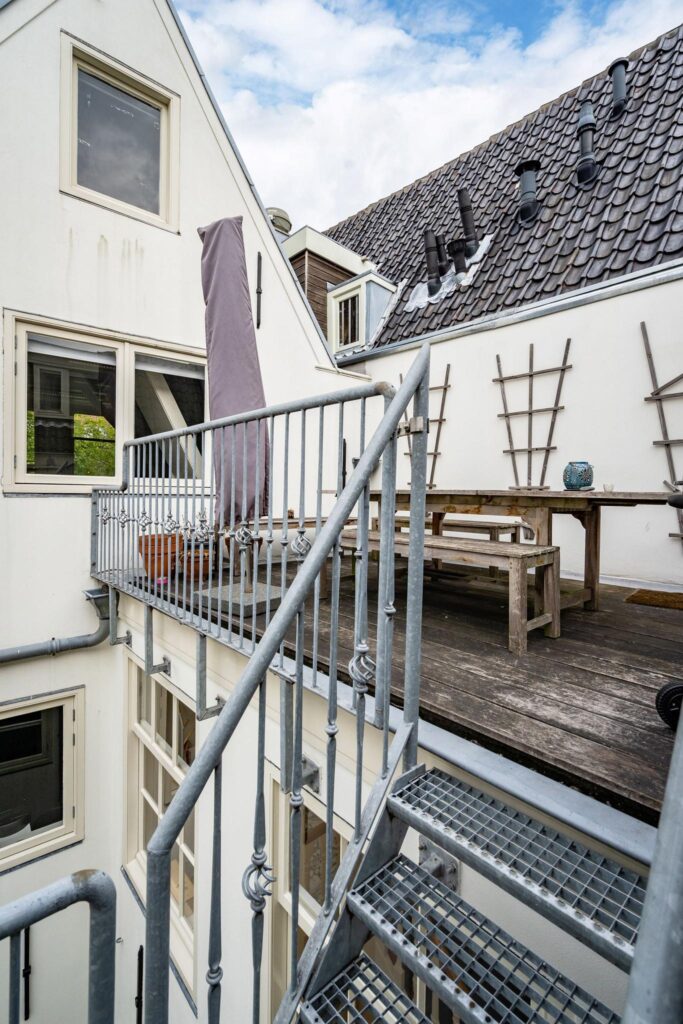 Buitenterras met houten tafel en metalen trap aan de achterzijde van een woning aan de Herengracht.