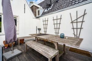 Houten dakterras met een verweerde picknicktafel, tuinbankjes en een gesloten parasol aan de Herengracht.