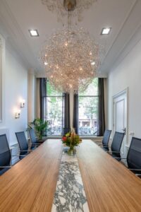 Stijlvolle vergaderruimte aan de Herengracht met moderne kroonluchter, lange houten tafel en uitzicht op de gracht.