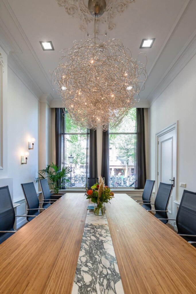 Stijlvolle vergaderruimte aan de Herengracht met moderne kroonluchter, lange houten tafel en uitzicht op de gracht.