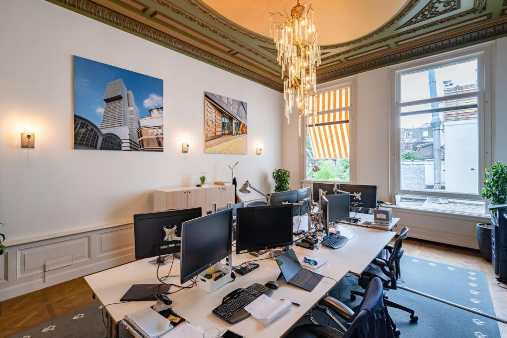 Modern kantoor met meerdere werkplekken in een klassiek grachtenpand aan de Herengracht, met hoge plafonds, kroonluchter en uitzicht op de stad.
