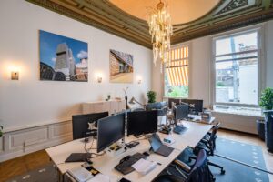 Modern kantoor met meerdere werkplekken in een klassiek grachtenpand aan de Herengracht, met hoge plafonds, kroonluchter en uitzicht op de stad.