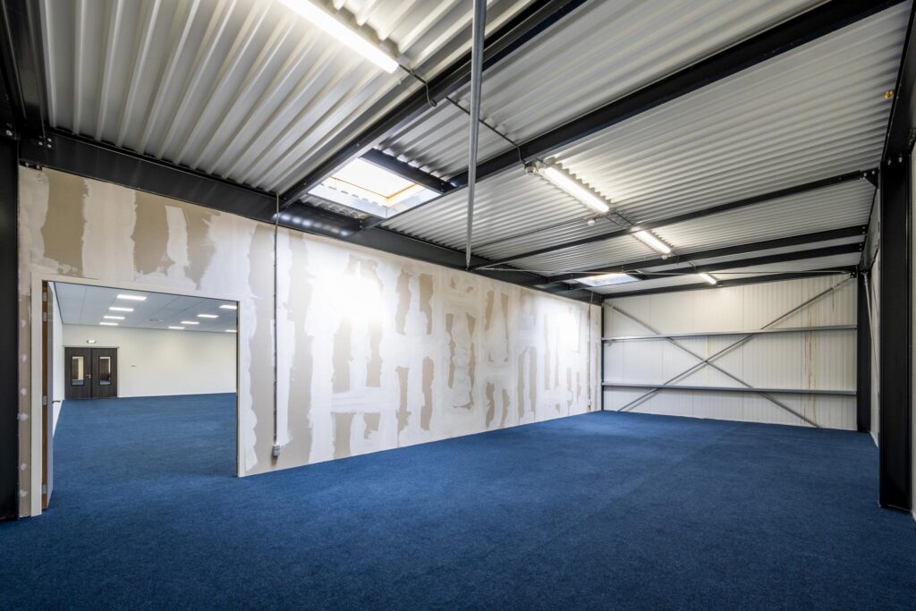Interior of a commercial unit on Dynamostraat with unfinished drywall, blue carpet, and exposed steel ceiling beams.