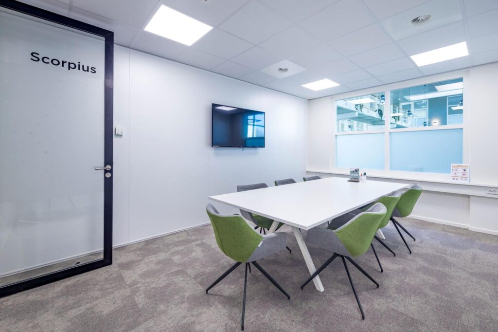 Vergaderruimte Scorpius met een witte tafel, zes stoelen, een flatscreen en grote ramen.