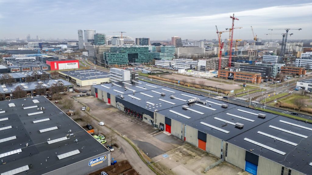 Luchtfoto van bedrijventerrein aan de Lemelerbergweg in Amsterdam-Zuidoost met kantoren, loodsen en bouwkranen op de achtergrond.