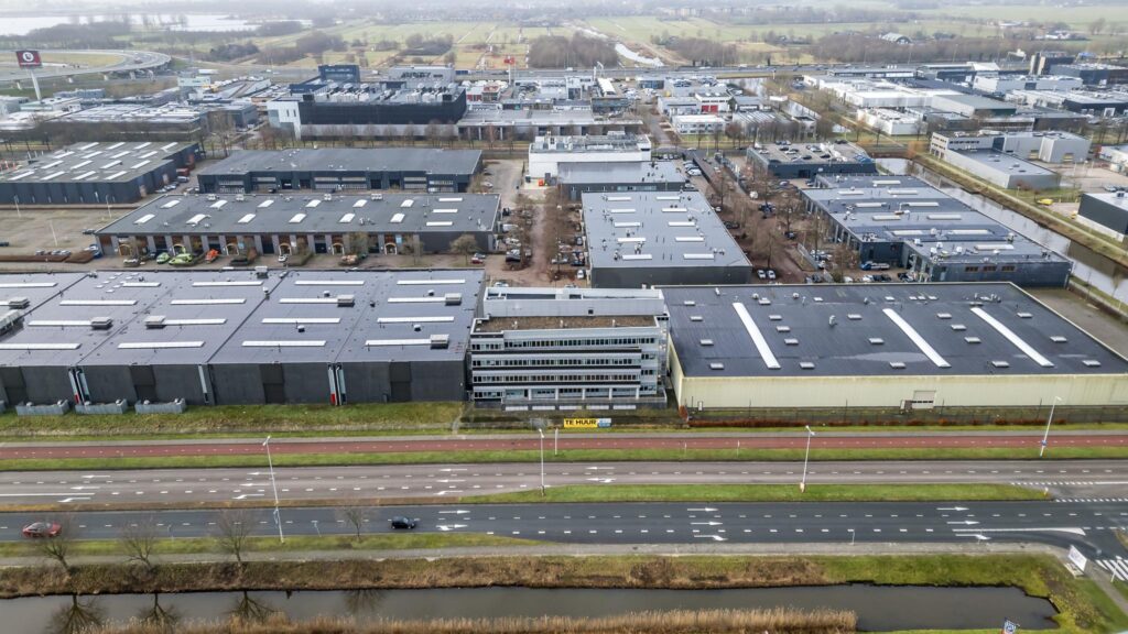 Luchtfoto van bedrijventerrein aan de Lemelerbergweg met magazijnen, kantoren en een "Te Huur" bord langs de weg.