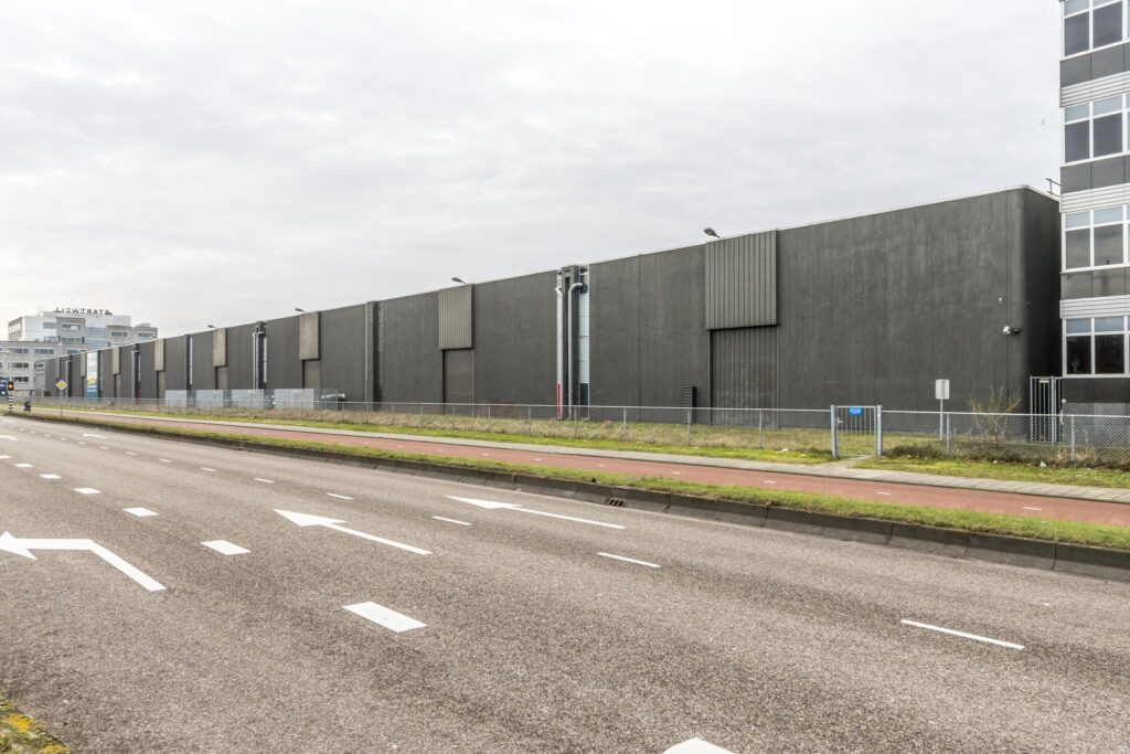 Grijze, moderne bedrijfs- of opslagloods aan de Lemelerbergweg in Amsterdam, gezien vanaf de weg.