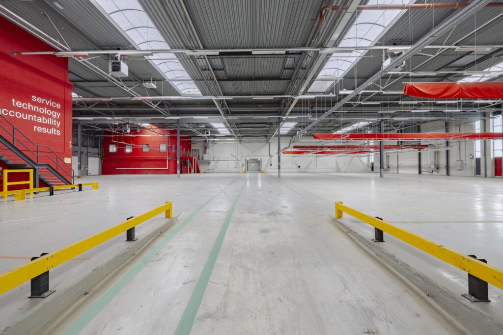 Ruime, lege bedrijfshal aan de Lemelerbergweg met rode accenten, gele veiligheidsrails en industriële details.