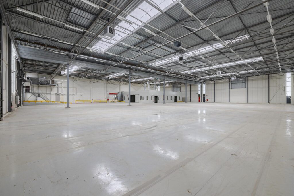 Ruime, lege bedrijfshal aan de Lemelerbergweg met een gladde vloer en metalen dakconstructie.