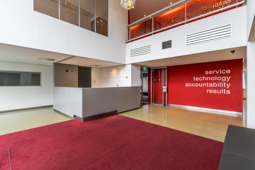 Moderne ontvangsthal aan de Lemelerbergweg met een rood accentmuur met kernwaarden en een balie van het bedrijf Intralox.