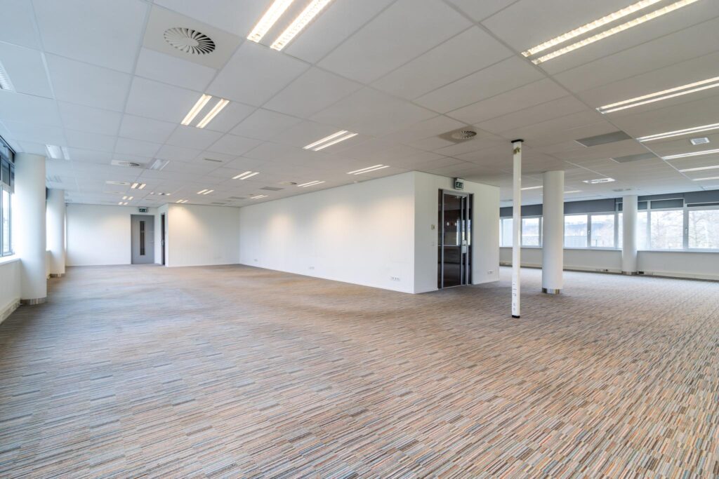 Ruime, lege kantoorruimte aan de Lemelerbergweg met tapijtvloer, systeemplafond en grote ramen.