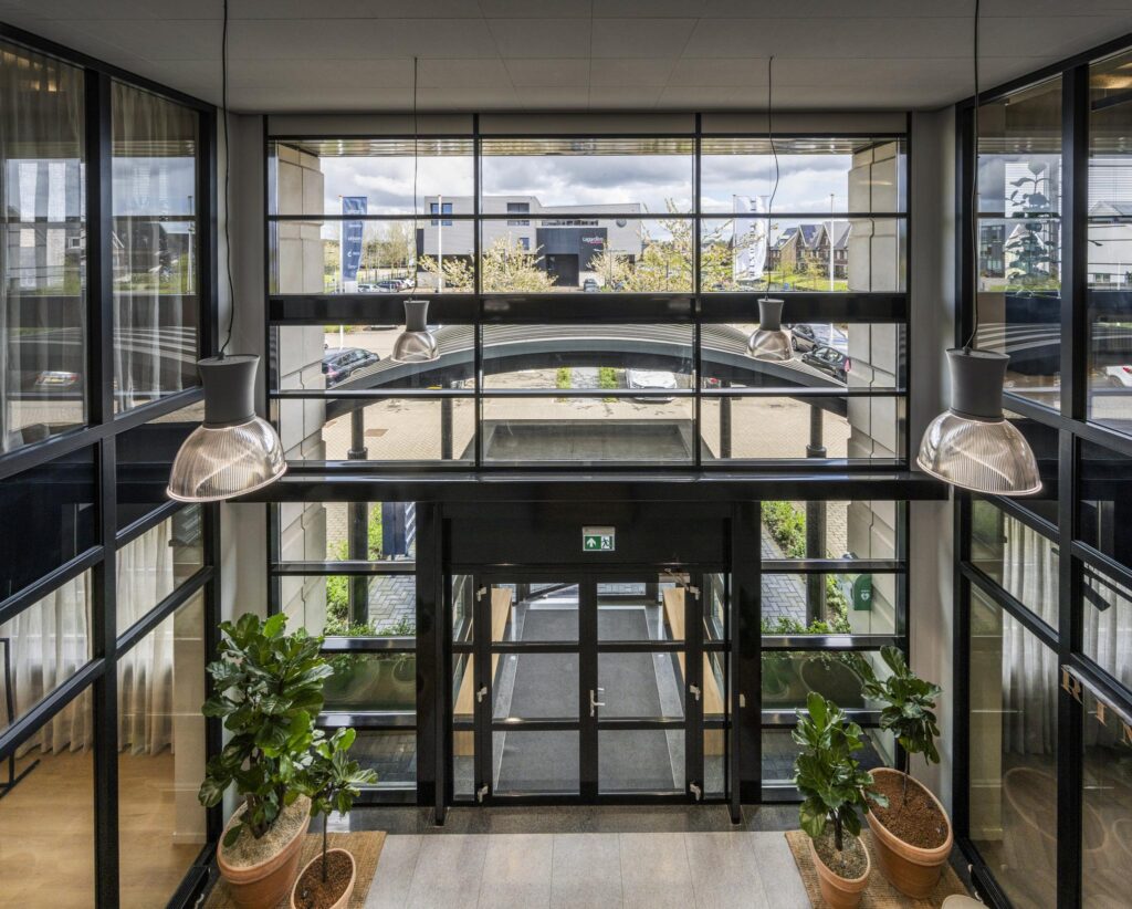 Modern glass entrance lobby with large windows, hanging lamps, and potted plants at Singaporestraat.