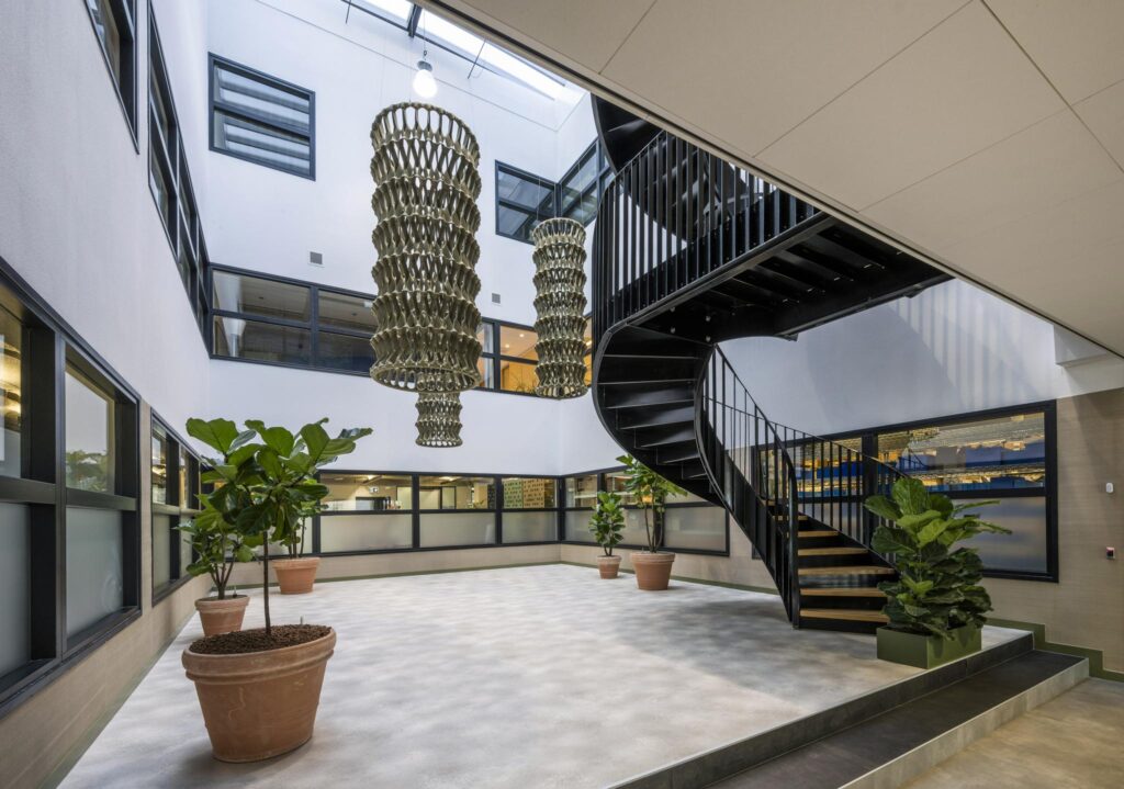 Modern atrium with large hanging chandeliers, a black spiral staircase, and potted plants at Singaporestraat.