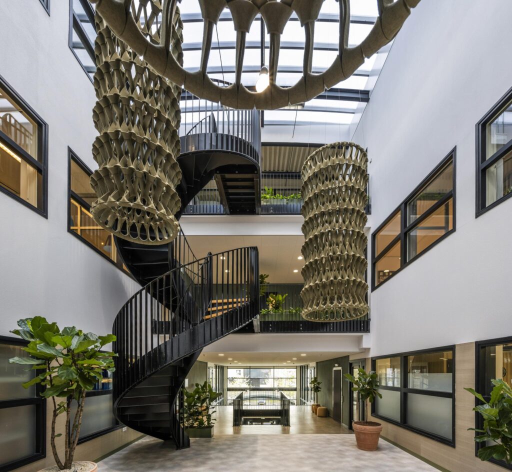 Modern atrium with a black spiral staircase, large hanging sculptures, and indoor plants at Singaporestraat.