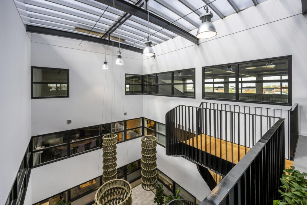 Modern atrium in an office building on Singaporestraat with black-framed windows, hanging light fixtures, and an open staircase.