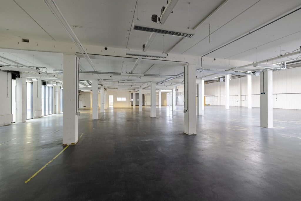 Ruime, lege industriële hal aan de Laarderhoogtweg met witte kolommen en betonnen vloer.