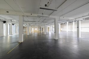 Ruime, lege industriële hal aan de Laarderhoogtweg met witte kolommen en betonnen vloer.
