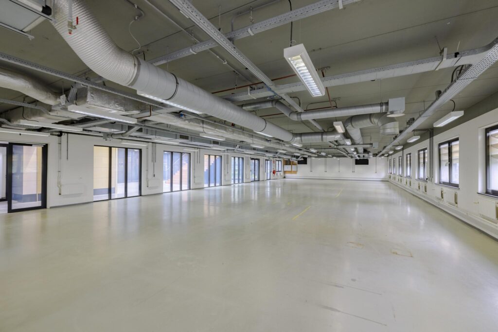 Leeg kantoorgebouw aan de Laarderhoogtweg met grote ramen en zichtbare ventilatiebuizen aan het plafond.