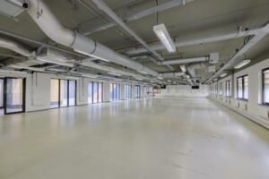 Leeg kantoorgebouw aan de Laarderhoogtweg met grote ramen en zichtbare ventilatiebuizen aan het plafond.