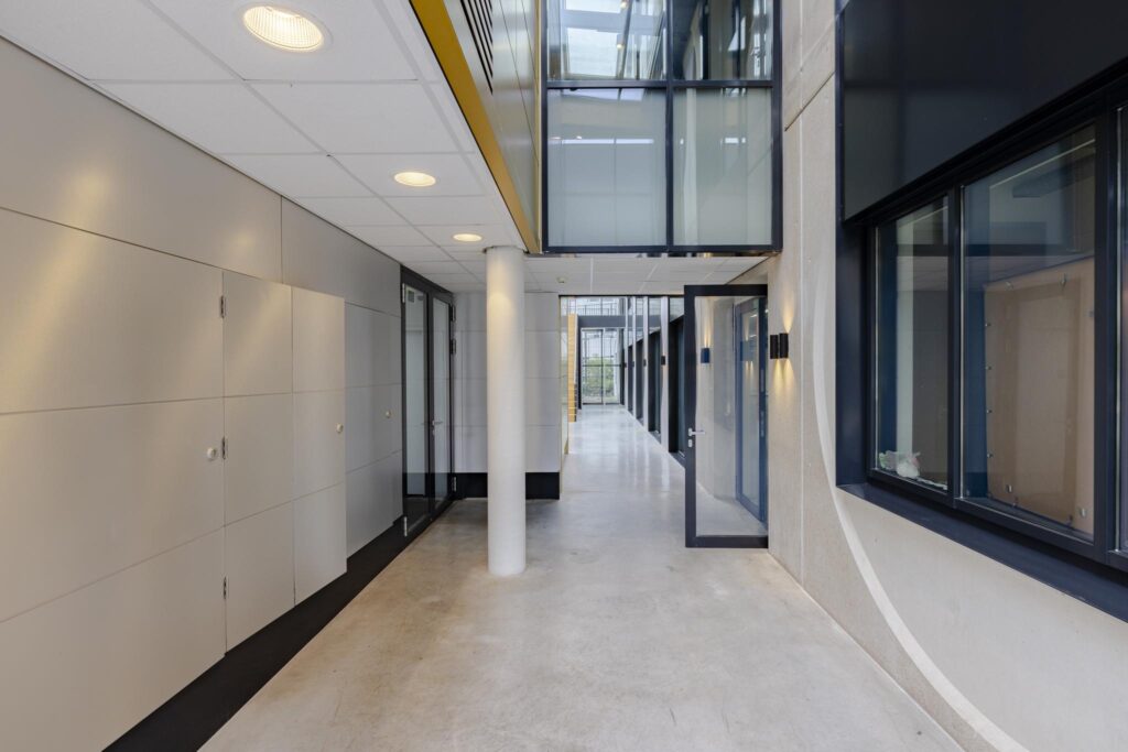 Moderne, lichte gang in een kantoorpand aan de Laarderhoogtweg met glazen deuren en betonnen vloer.