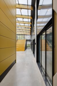 Moderne lichte entree met glazen dak, houten trap en gele wand aan de Laarderhoogtweg.