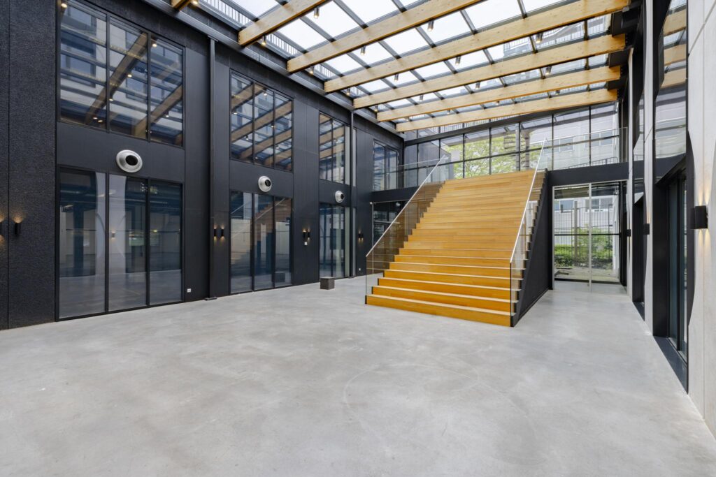 Moderne, open entreehal met glazen dak en brede houten trap aan de Laarderhoogtweg.