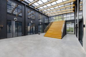 Moderne, open entreehal met glazen dak en brede houten trap aan de Laarderhoogtweg.