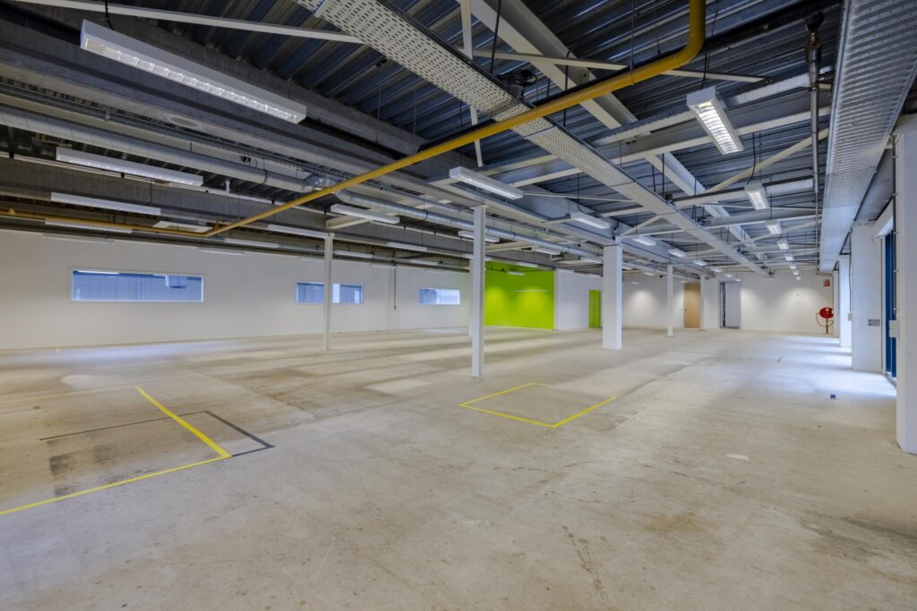 Leeg bedrijfsruimte aan de Laarderhoogtweg met betonnen vloer, zichtbare plafonds en een felgroene accentmuur.